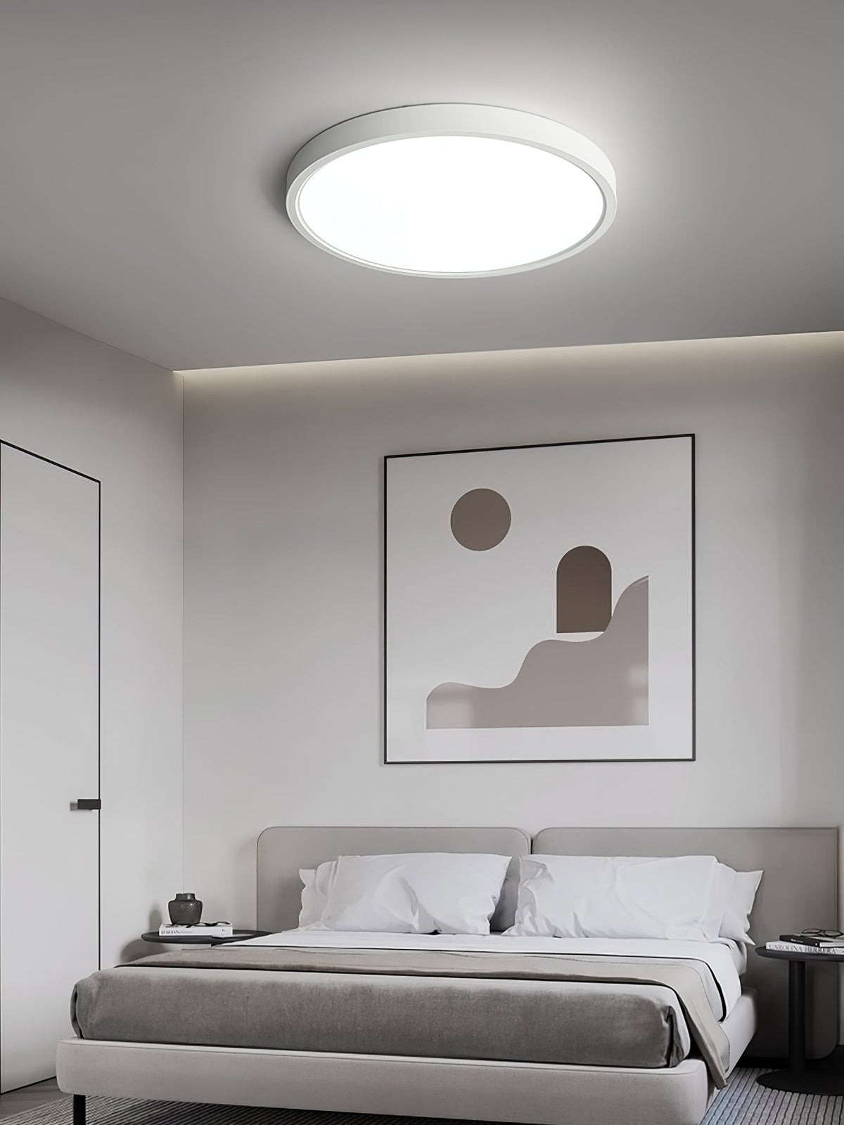 A white Clérachic round ceiling light glows above a grey bed with white pillows, beneath a framed abstract print.