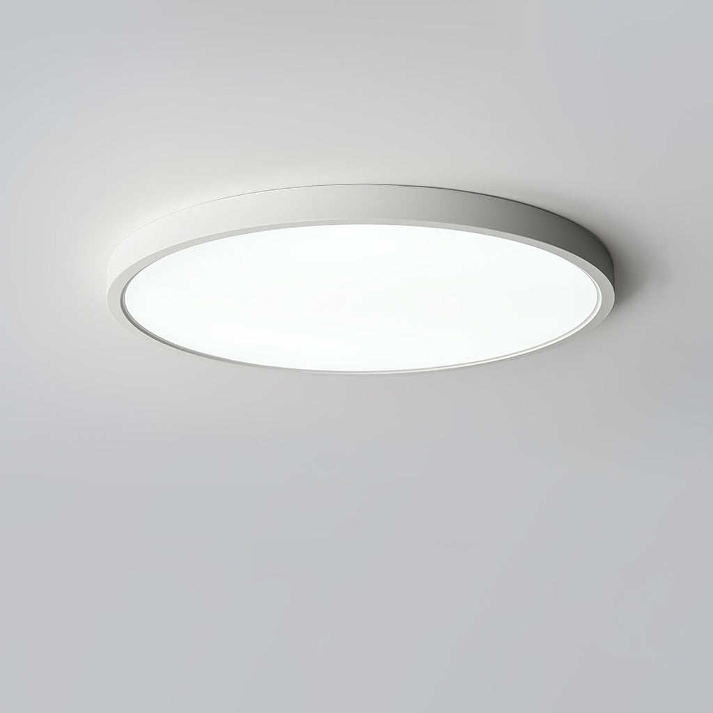 A white Clérachic slim round ceiling light shines bright white from a pale grey ceiling, its thin rim catching the light.