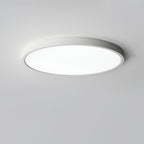 A white Clérachic slim round ceiling light shines bright white from a pale grey ceiling, its thin rim catching the light.