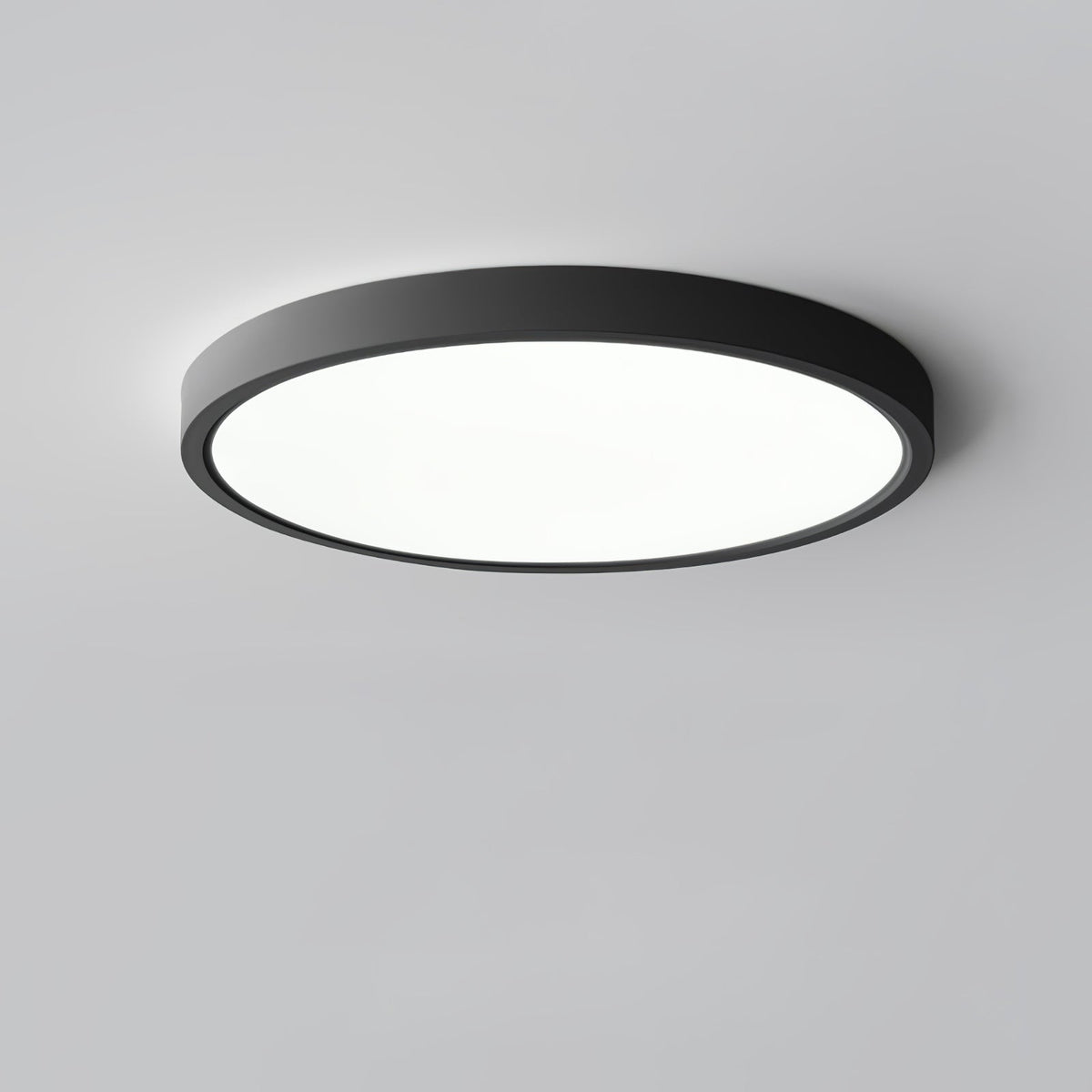 A black Clérachic round ceiling light with a flat white diffuser and a thin black rim, against a plain grey ceiling.