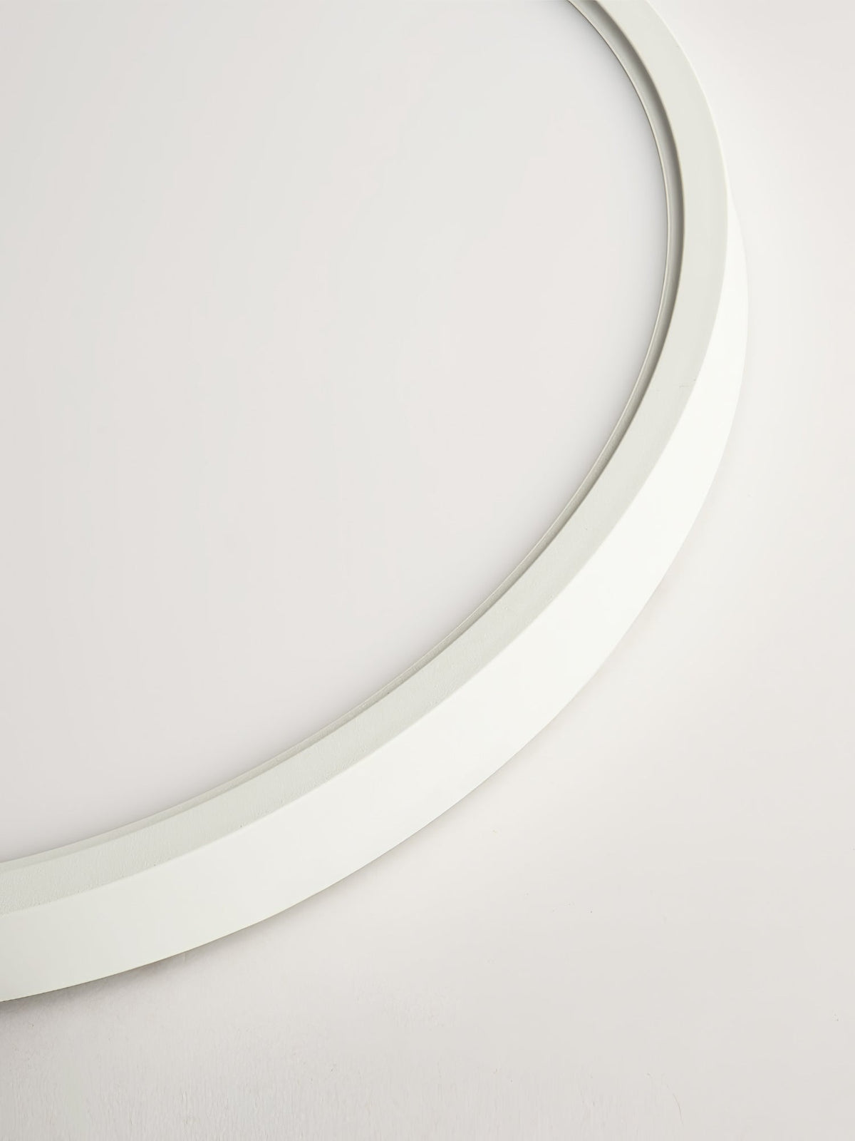 Close view of the thin curved white edge of this Clérachic ceiling light, with the soft glow of the diffuser along its inner lip.