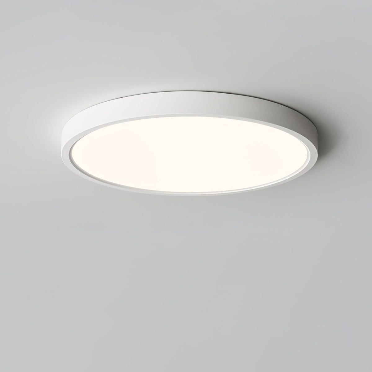 A white Clérachic round ceiling light glowing with a soft warm tone, seen from slightly below on a grey ceiling.