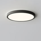 A black Clérachic round ceiling light lit with a soft warm glow, its slim rim visible against a pale grey ceiling.