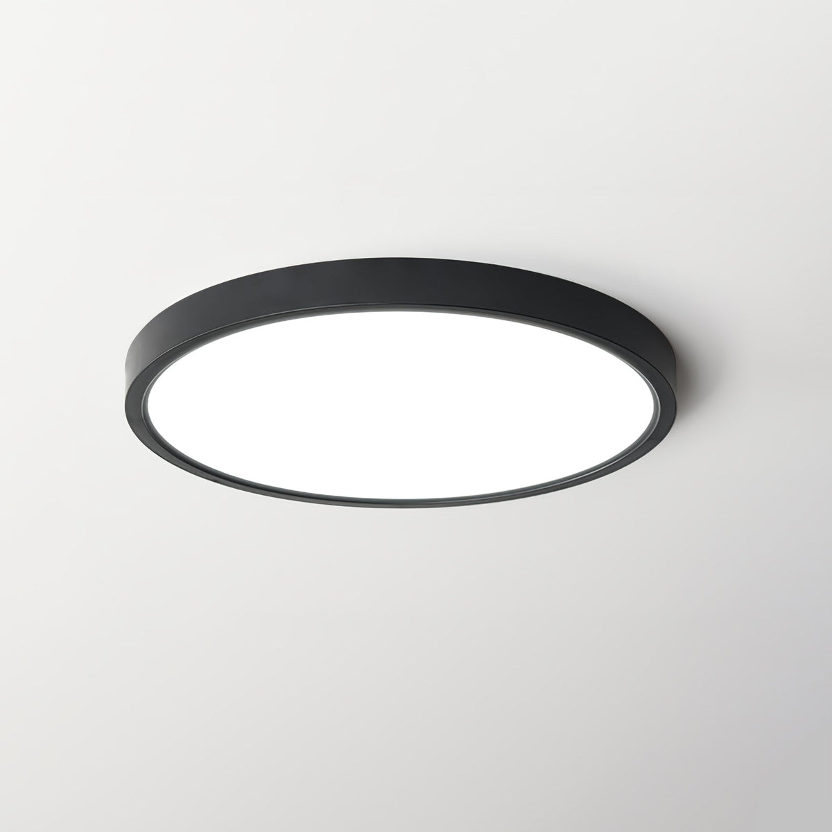 A black-rimmed Clérachic round ceiling light with a bright diffuser, centred on a light grey ceiling.