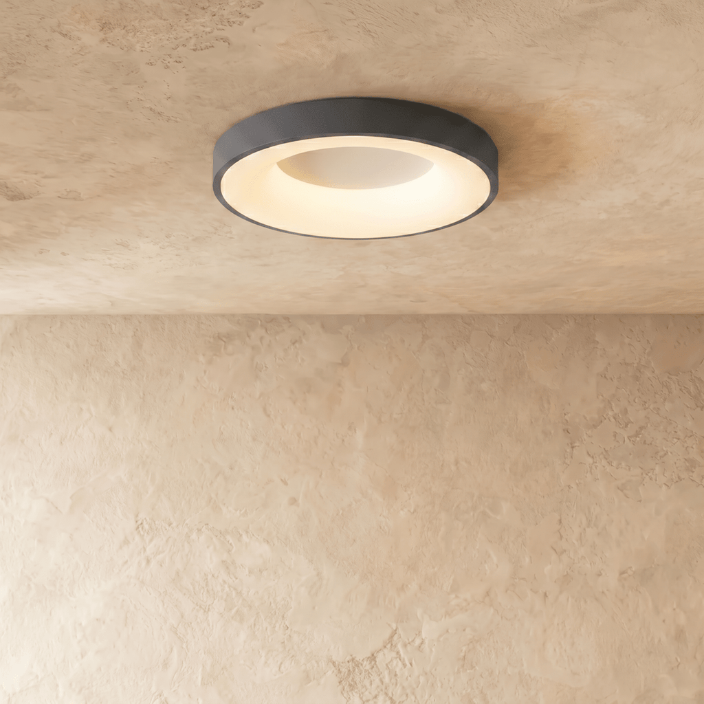 Clérachic grey round ceiling light, lit warm white, with a glowing inner ring on a textured limewash ceiling.