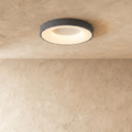 Clérachic grey round ceiling light, lit warm white, with a glowing inner ring on a textured limewash ceiling.