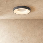 Clérachic grey round ceiling light, lit warm white, with a glowing inner ring on a textured limewash ceiling.