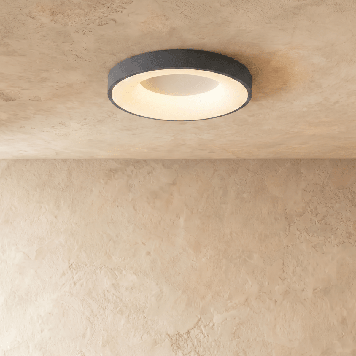 Clérachic grey round ceiling light, lit warm white, with a glowing inner ring on a textured limewash ceiling.
