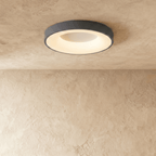 Clérachic grey round ceiling light, a slightly larger size, lit warm white above a softly textured plaster wall.
