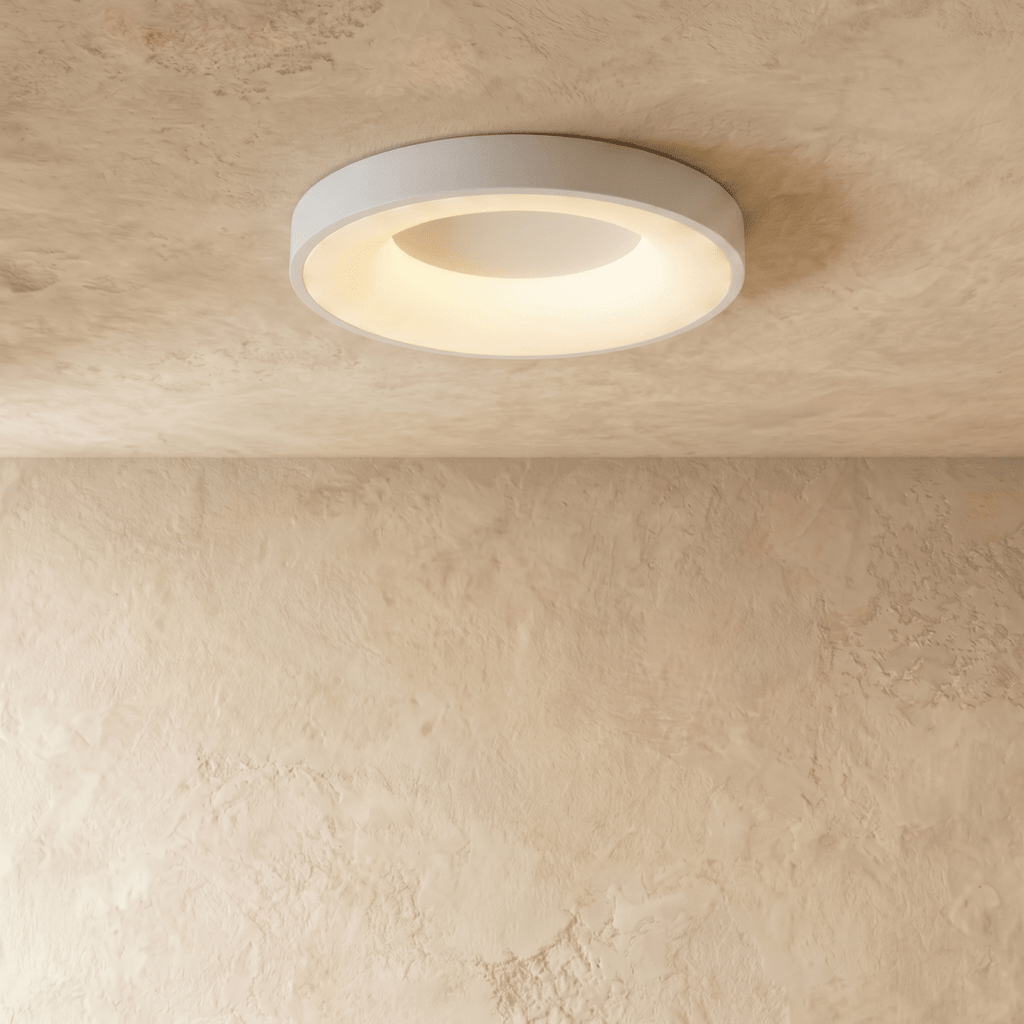 Clérachic white round ceiling light in a slightly larger size, lit warm white over a plaster wall.