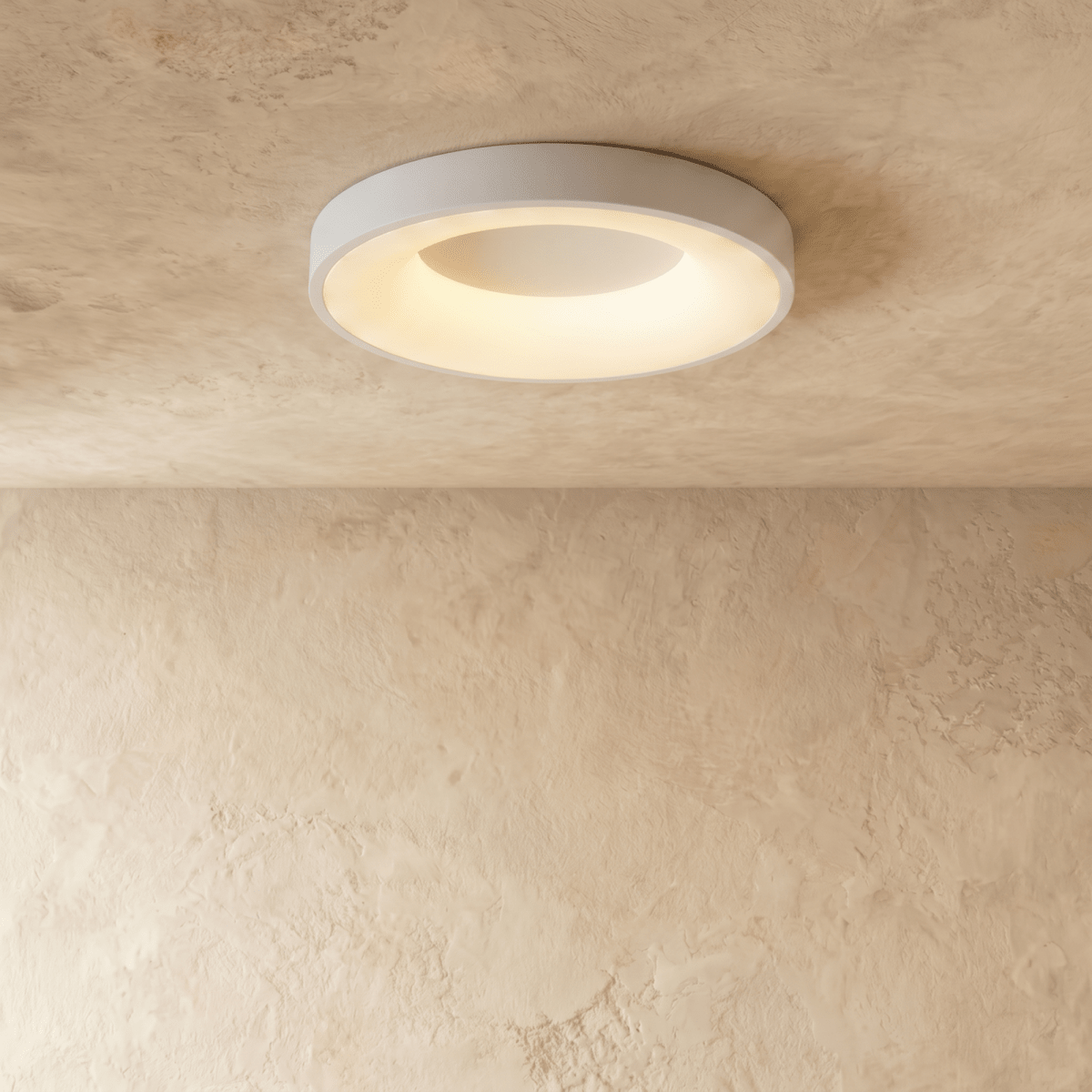 Clérachic white round ceiling light in a slightly larger size, lit warm white over a plaster wall.