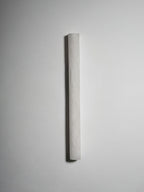 Unlit slim sconce on a grey wall, its pale alabaster surface showing a faint hand-finished texture; a Clérachic wall light.