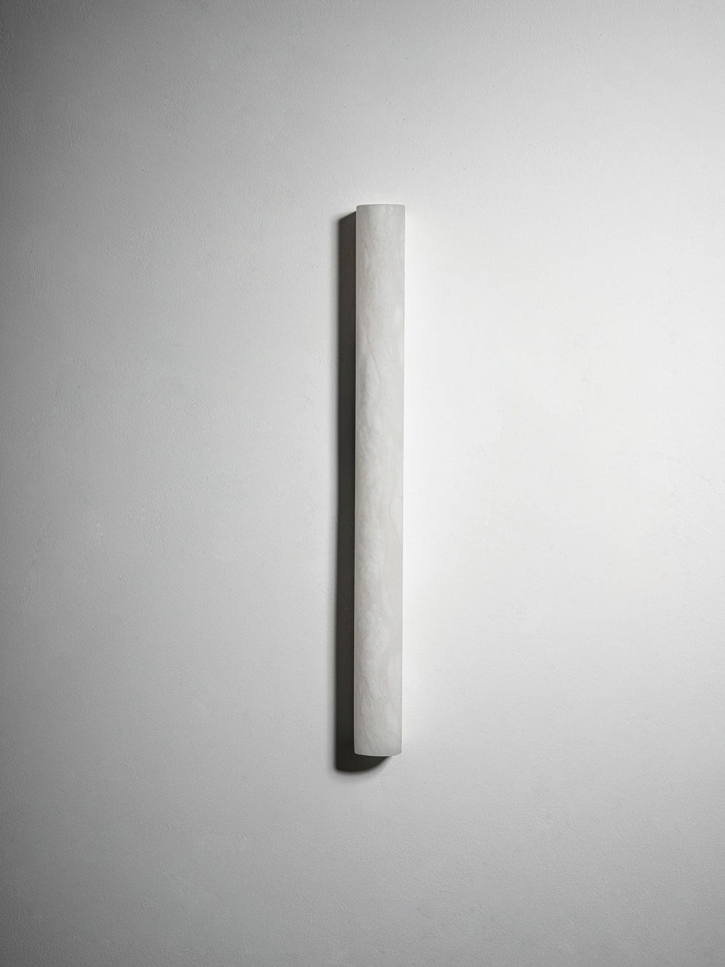 The longer Clérachic alabaster sconce seen from a slight angle on a light wall, unlit, its curved pale face dimly textured.