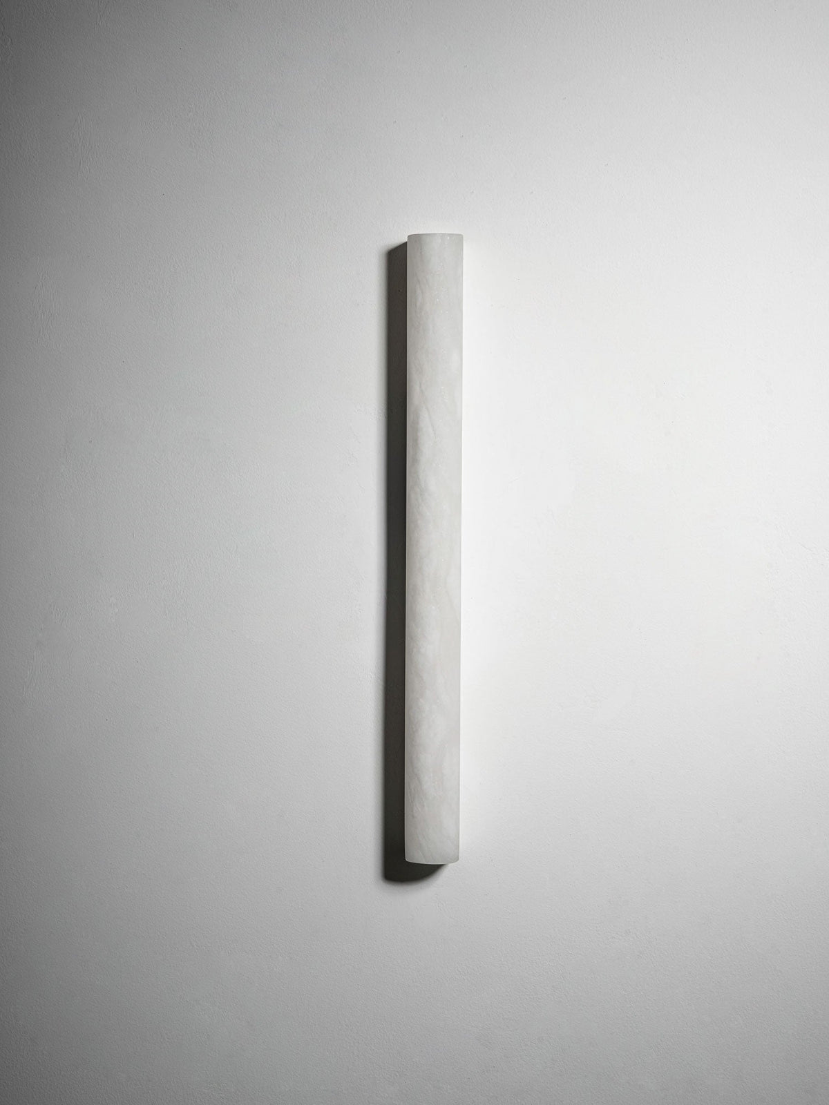 The longer Clérachic alabaster sconce seen from a slight angle on a light wall, unlit, its curved pale face dimly textured.