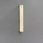 Lit Clérachic sconce on a mid-grey wall, a bright strip of glowing alabaster with soft marbling inside its slim form.