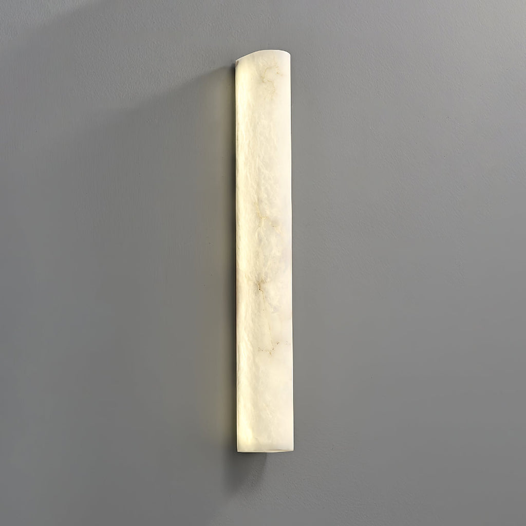 Close view of the glowing alabaster sconce on a grey wall, the creamy veins lit from behind and a gentle shadow below; Clérachic.