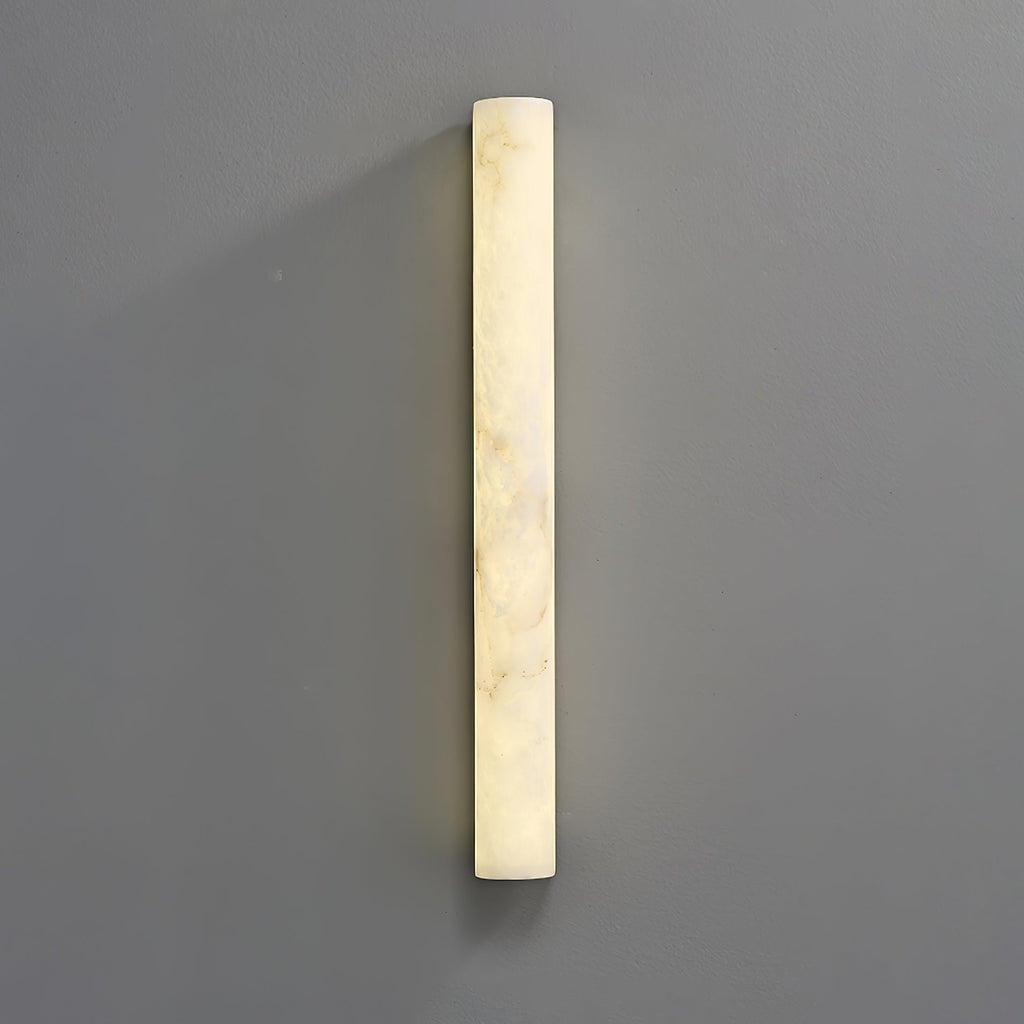A tall lit alabaster sconce on a grey wall, its glow brightest down the left edge and cloudy veins across the face; from Clérachic.
