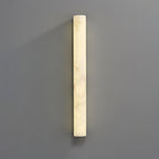 A tall lit alabaster sconce on a grey wall, its glow brightest down the left edge and cloudy veins across the face; from Clérachic.
