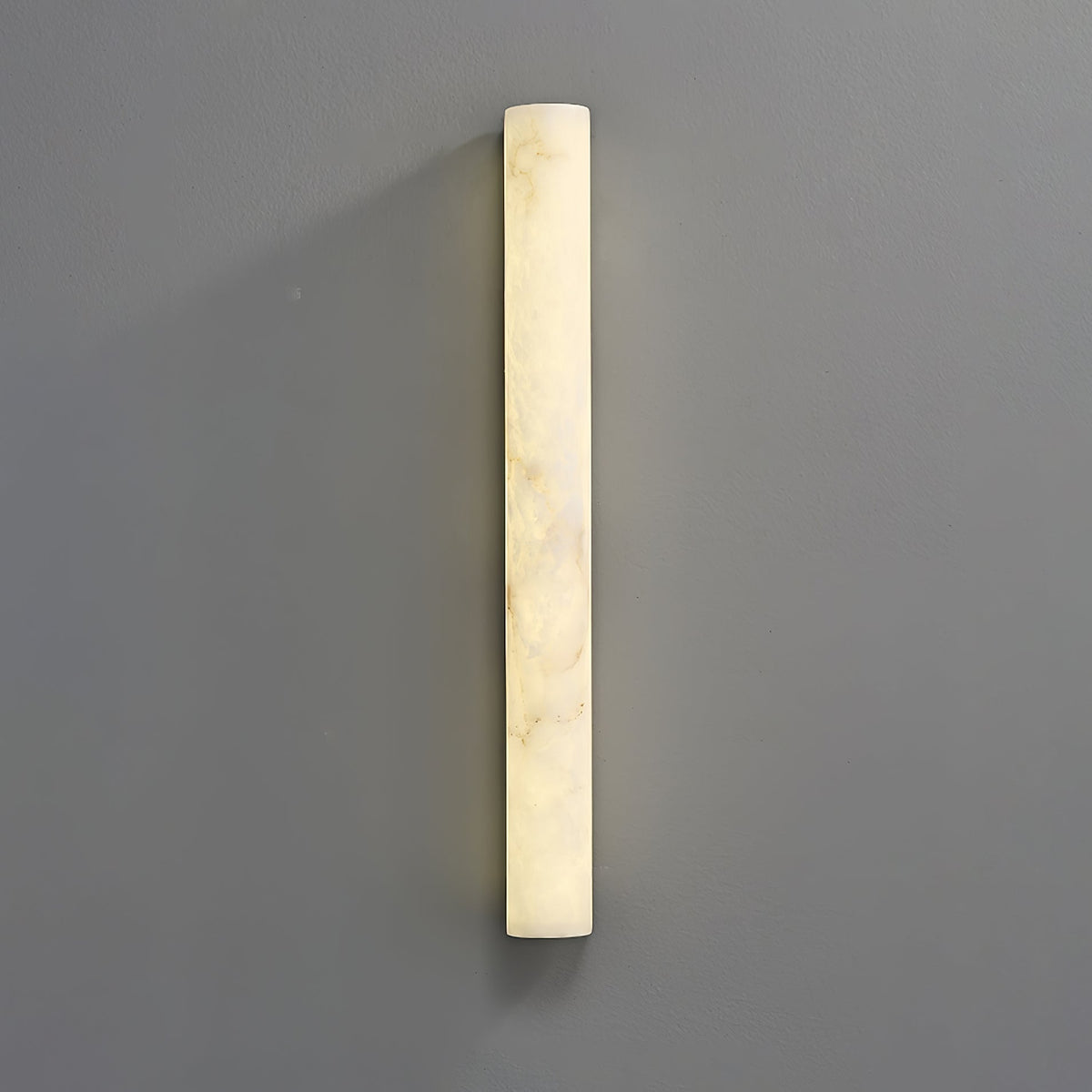 A tall lit alabaster sconce on a grey wall, its glow brightest down the left edge and cloudy veins across the face; from Clérachic.