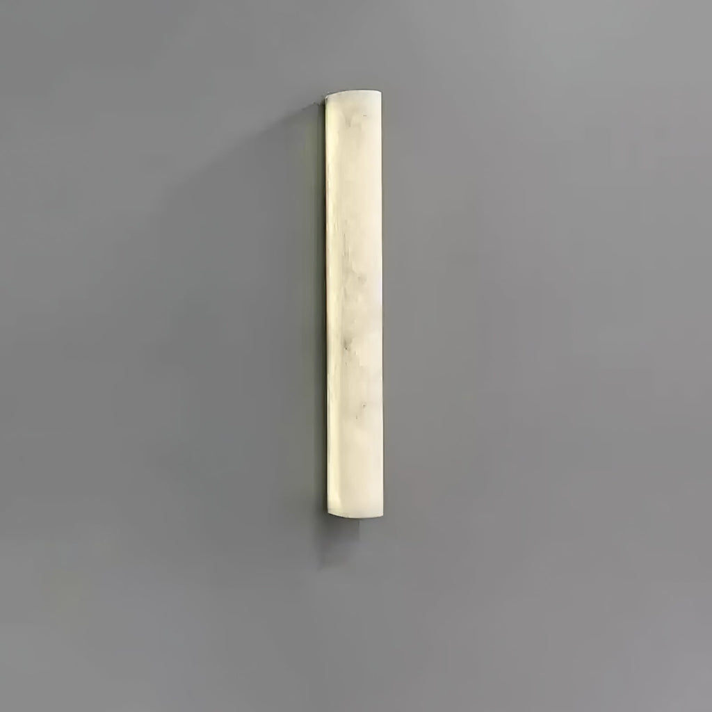 Shorter Clérachic sconce lit on a grey wall, the creamy alabaster face glowing evenly with soft marbling.