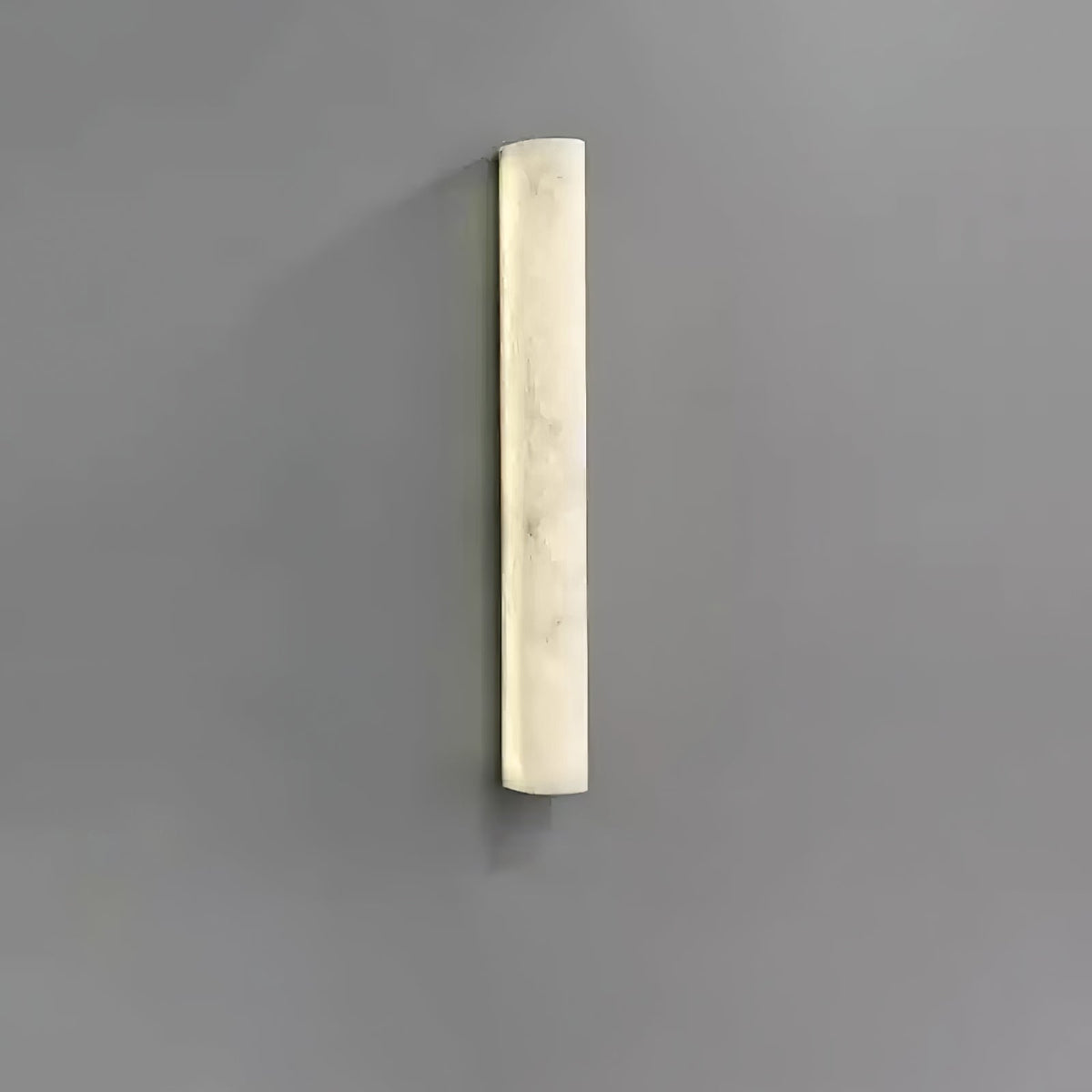 Shorter Clérachic sconce lit on a grey wall, the creamy alabaster face glowing evenly with soft marbling.