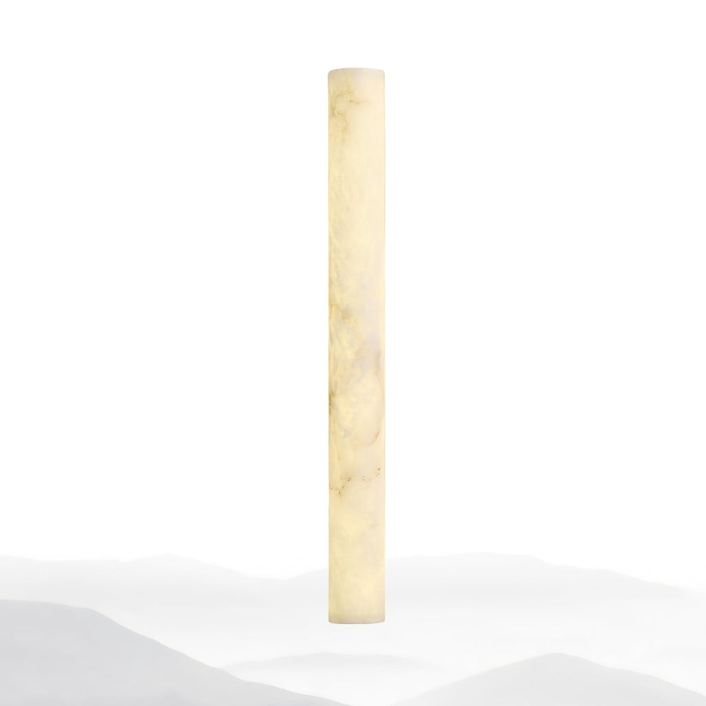 Slim alabaster column lit warm cream against a white backdrop with faint misty hills at its foot; this Clérachic wall light.