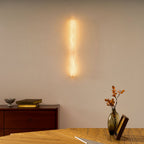 This Clérachic sconce glows warm on a cream wall above a wooden desk with a vase of dried stems and a framed picture.