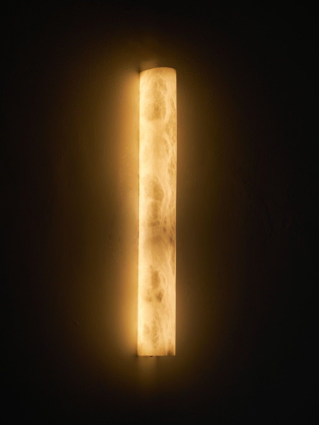 Bright cloudy alabaster glowing amber and cream on a dark wall, a halo of warm light around the Clérachic sconce.