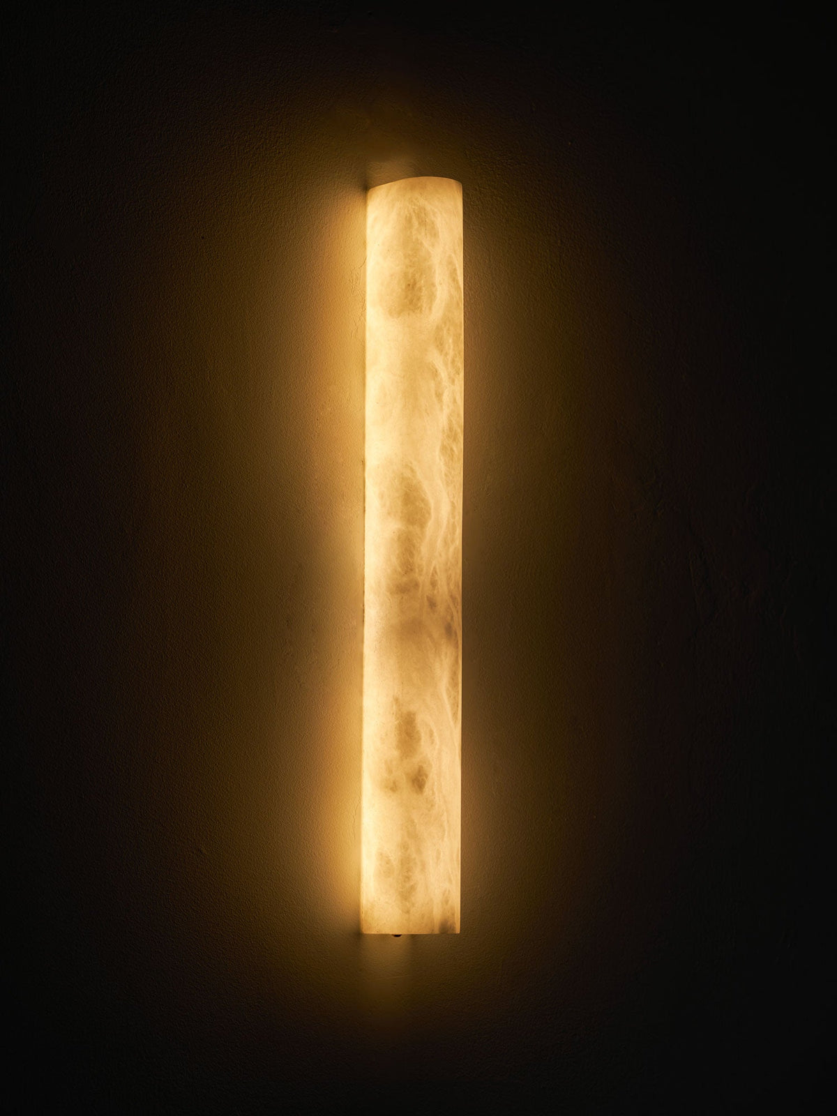 Bright cloudy alabaster glowing amber and cream on a dark wall, a halo of warm light around the Clérachic sconce.