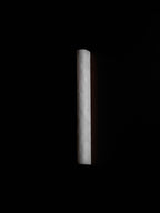 White alabaster sconce unlit in a pitch-dark scene, the pale stone catching a little light along its edge; from Clérachic.