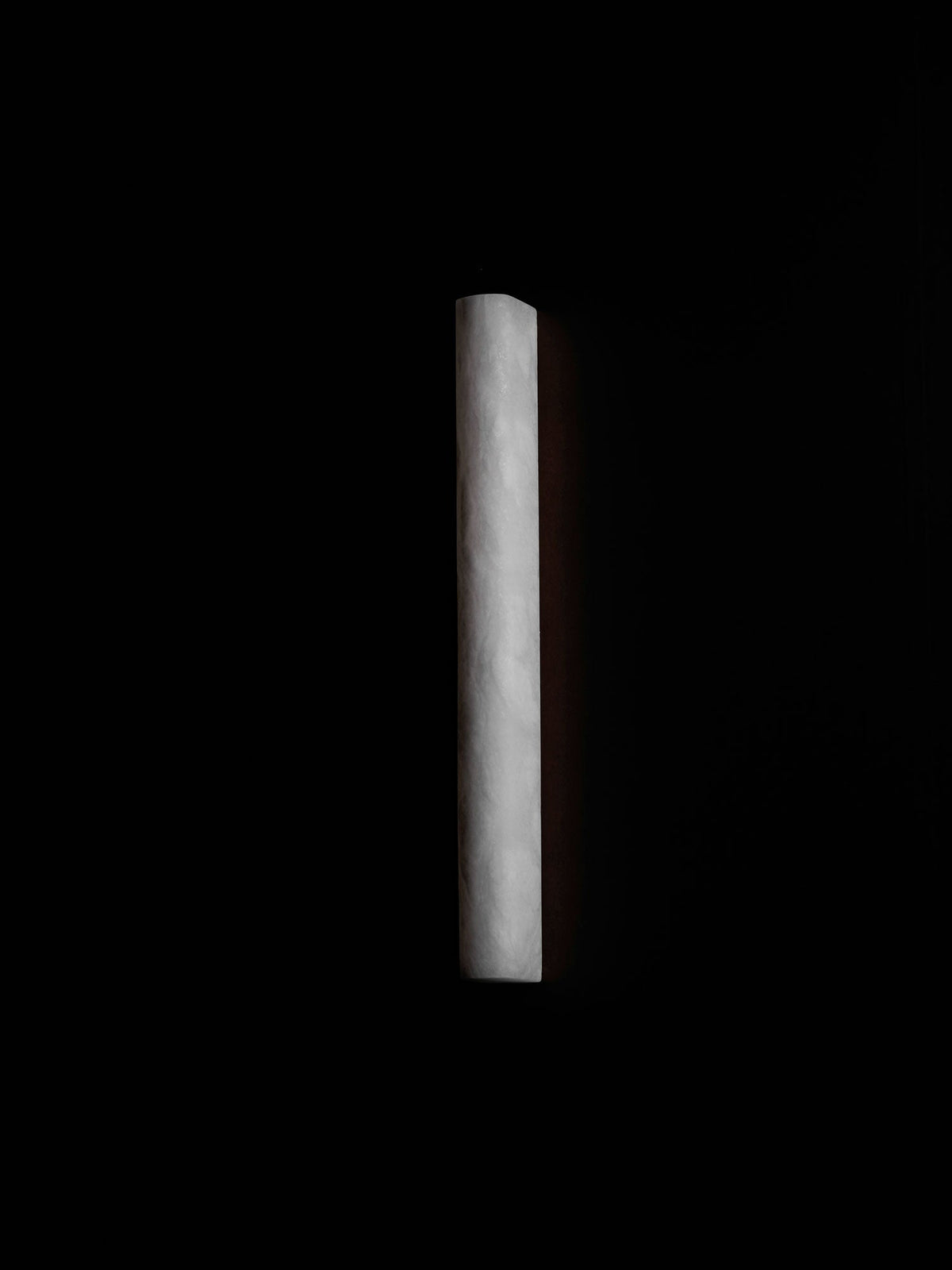 White alabaster sconce unlit in a pitch-dark scene, the pale stone catching a little light along its edge; from Clérachic.