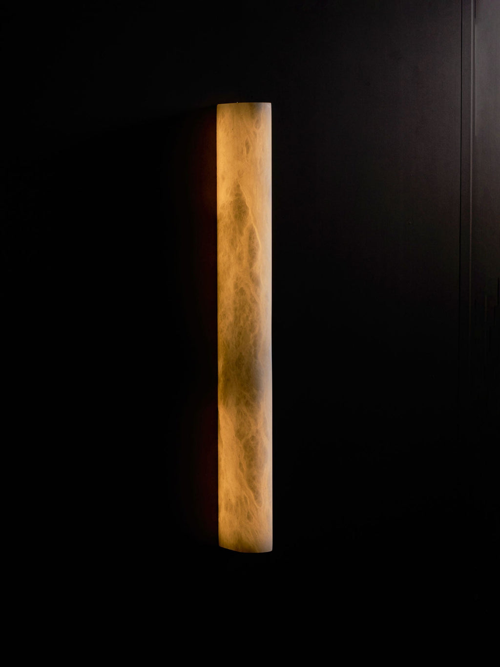 Warm amber light through an alabaster sconce on a dark wall, the clouded stone pattern clear in its face; this Clérachic design.