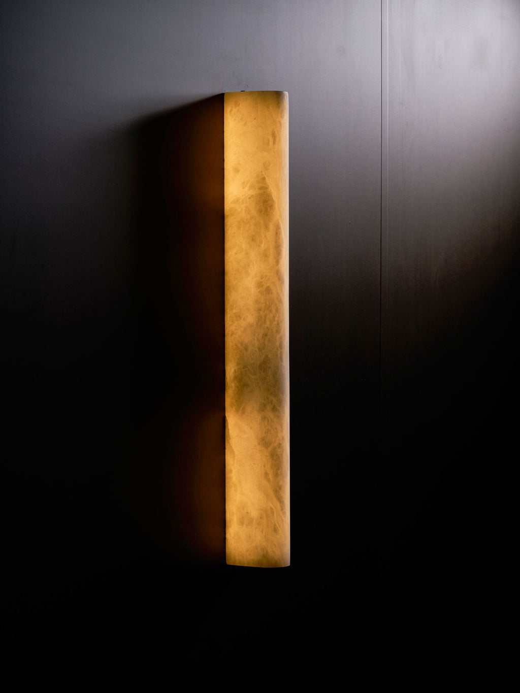 Close view of the Clérachic sconce lit on a dark wall with a pale beam of light across the upper right corner.