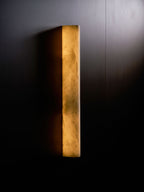 Close view of the Clérachic sconce lit on a dark wall with a pale beam of light across the upper right corner.