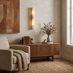 Beside a tall window, this lit Clérachic alabaster wall light hangs above a walnut sideboard with books, a vase and a cream armchair.