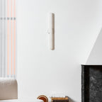 Unlit Clérachic alabaster wall light high on a white wall above a boucle sofa corner and a dark stone fireplace surround.