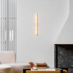 The glowing Clérachic alabaster wall light on a pale wall, seen above a cream sofa, a cup and saucer and a stone fireplace.