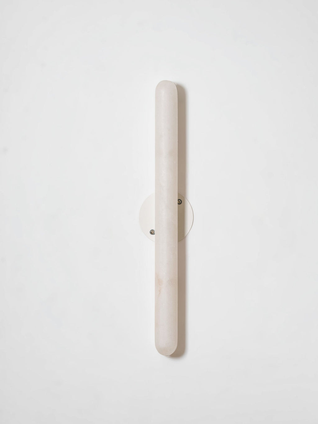 Unlit Clérachic alabaster wall light on a pale wall, showing the pale stone cylinder and its small round metal backplate.