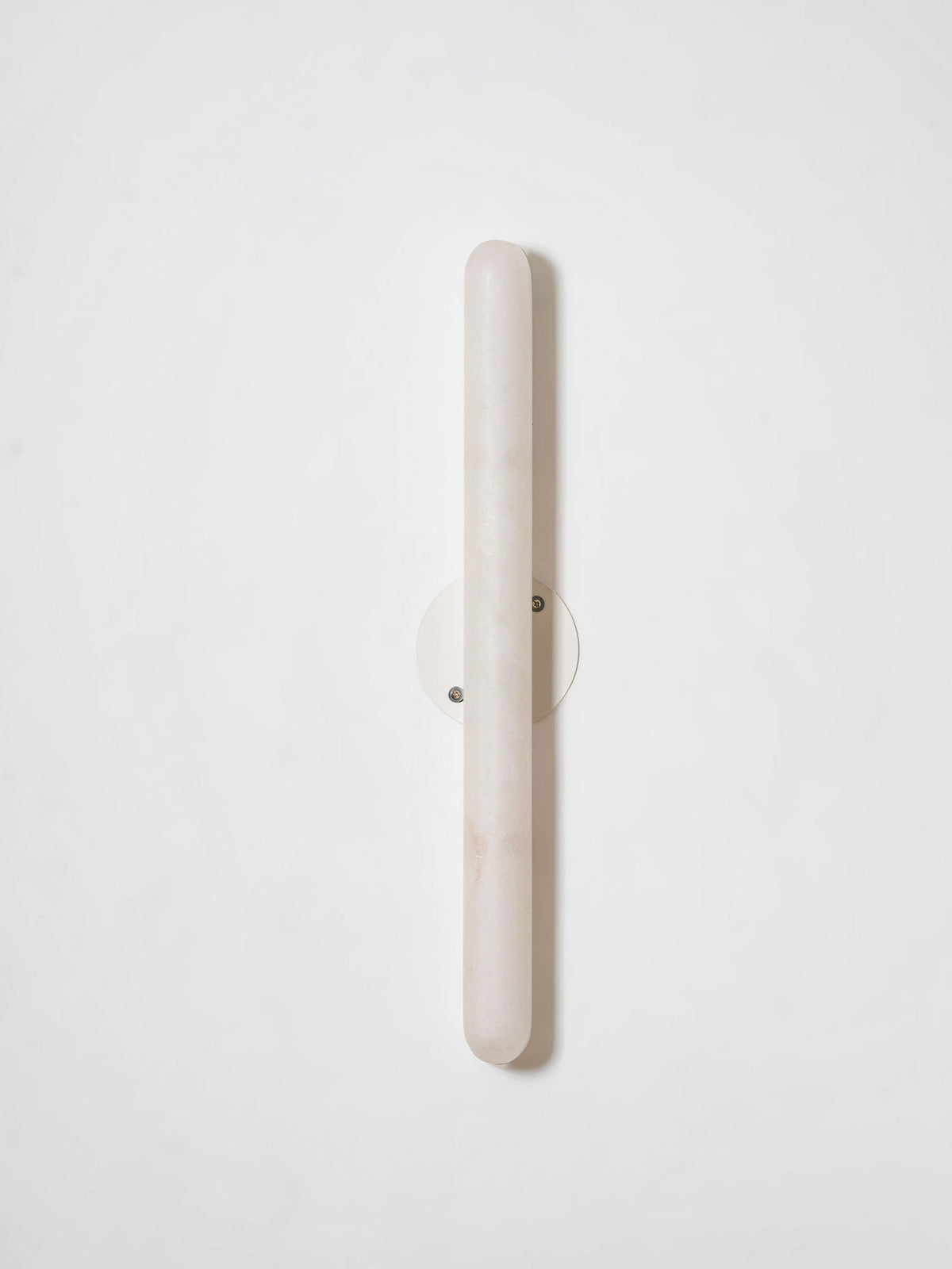 Unlit Clérachic alabaster wall light on a pale wall, showing the pale stone cylinder and its small round metal backplate.