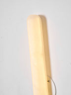 Close view of the rounded top end of this Clérachic alabaster wall light, glowing warm beside its small round backplate.