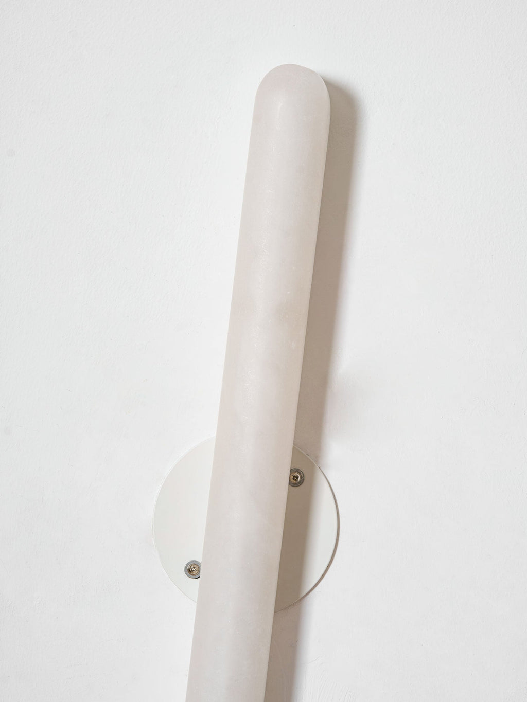 Angled view of the unlit Clérachic alabaster wall light, with its pale veined stone and the round white backplate behind it.