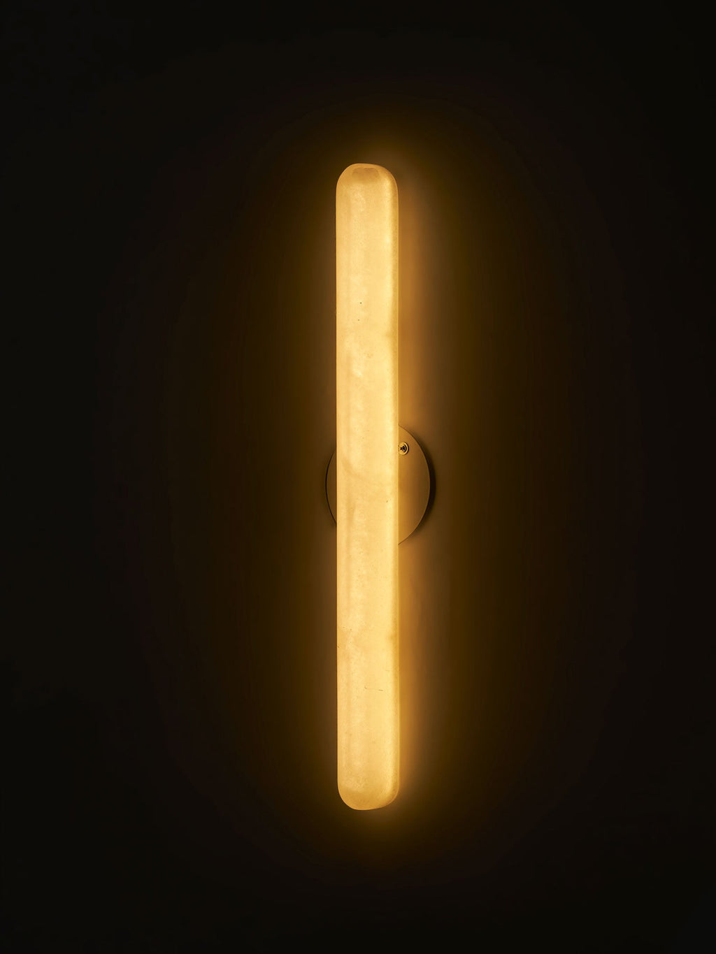 Close-framed Clérachic alabaster wall light lit in a dark room, the translucent cylinder glowing gold from end to end.