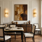 Pair of lit Clérachic alabaster wall lights flanking a framed abstract painting above a sideboard and a set dining table.