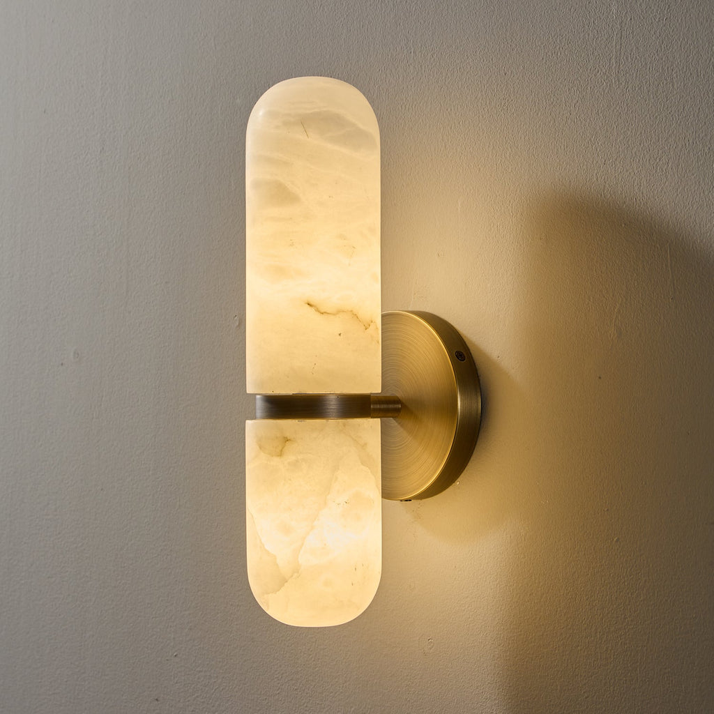 Close view of the lit Clérachic alabaster wall light in a bronze and white finish, light glowing through the veined stone.
