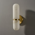 Clérachic alabaster wall light, unlit, on a grey wall, with a brass band and round brass backplate casting a shadow.