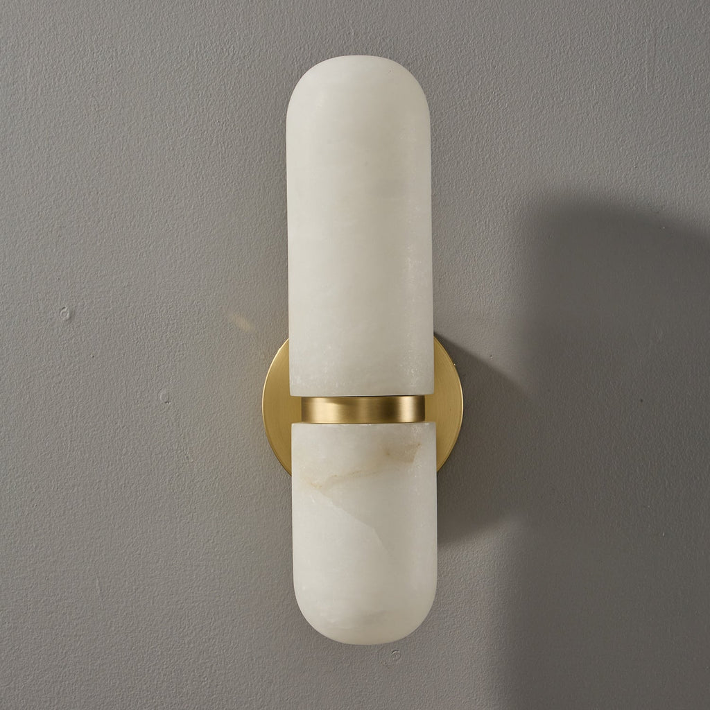Front view of the unlit Clérachic alabaster wall light, with a pill-shaped shade split by a brass band over the round backplate.