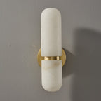 Front view of the unlit Clérachic alabaster wall light, with a pill-shaped shade split by a brass band over the round backplate.