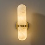 Lit Clérachic alabaster wall light seen from the front, a warm glow through the white veined stone and the brass band.