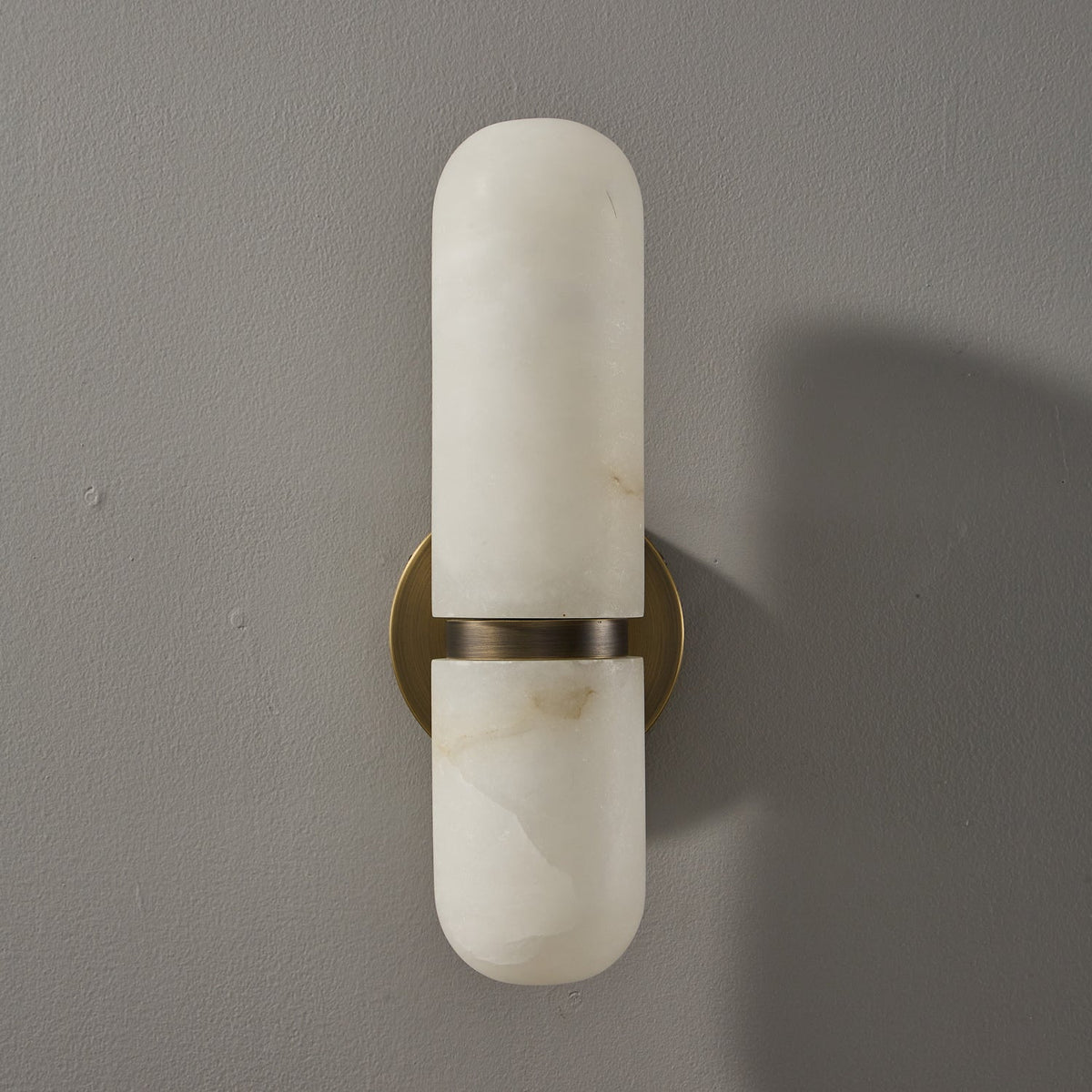 Front view of the bronze and white Clérachic alabaster wall light, unlit, on a grey wall with a soft shadow.