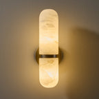 Close view of the lit Clérachic alabaster wall light, with golden veins showing in the glowing stone around the brass band.